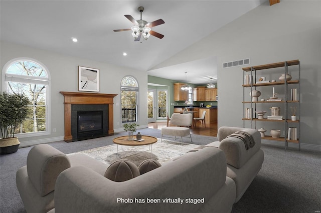 carpeted living room with a healthy amount of sunlight, ceiling fan with notable chandelier, and high vaulted ceiling