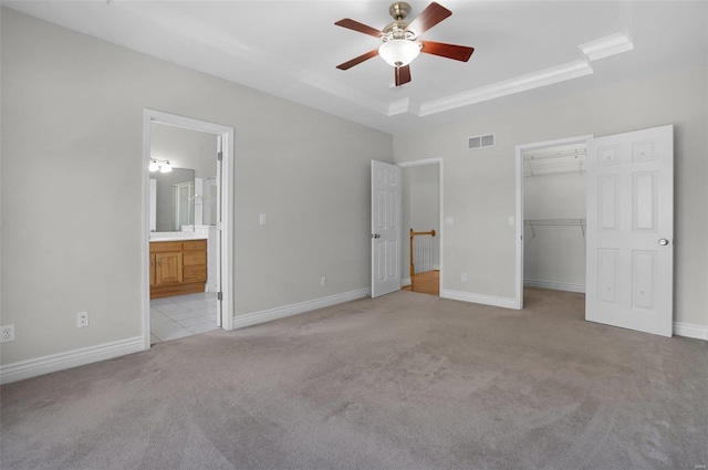 unfurnished bedroom with a walk in closet, a tray ceiling, light carpet, ensuite bath, and a closet