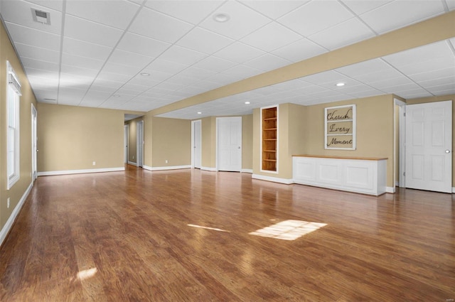 unfurnished living room with wood-type flooring, a paneled ceiling, and built in shelves