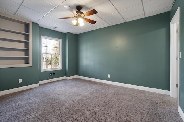 empty room with a paneled ceiling, built in features, ceiling fan, and carpet