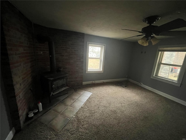 unfurnished living room with a wood stove, light colored carpet, and ceiling fan