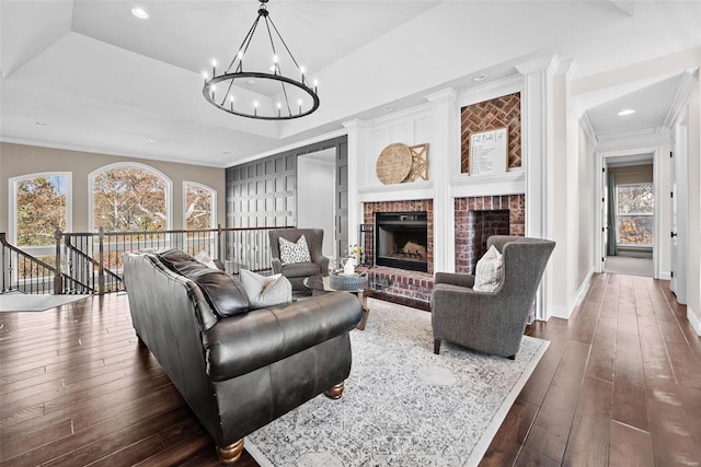 living room with an inviting chandelier, dark hardwood / wood-style floors, a tray ceiling, a fireplace, and ornamental molding