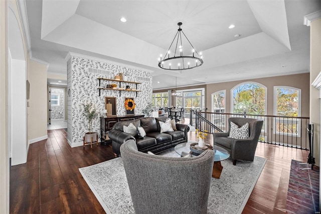 living room featuring an inviting chandelier, dark wood-type flooring, ornamental molding, and a raised ceiling