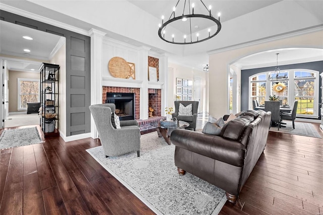 living room featuring dark wood-type flooring, a fireplace, crown molding, and a notable chandelier