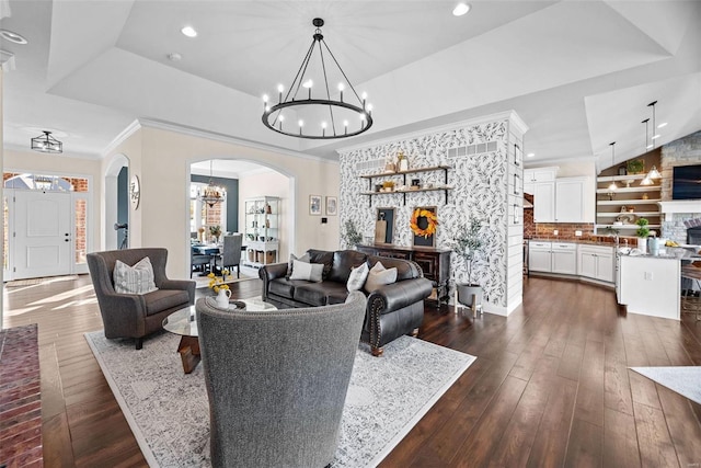 living room featuring a raised ceiling, crown molding, dark hardwood / wood-style floors, and an inviting chandelier