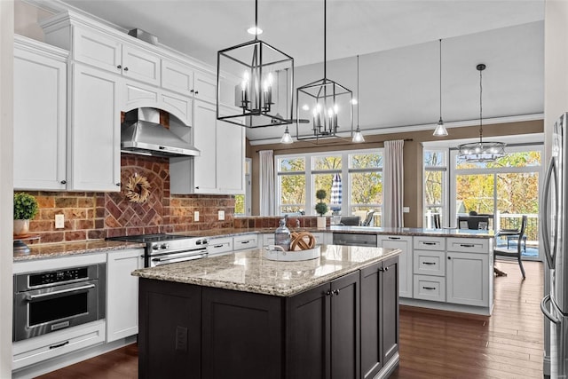 kitchen with hanging light fixtures, stainless steel appliances, white cabinets, a kitchen island, and wall chimney exhaust hood