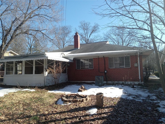 snow covered back of property featuring a sunroom