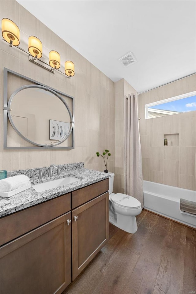 full bathroom featuring tile walls, hardwood / wood-style flooring, vanity, toilet, and shower / bath combo