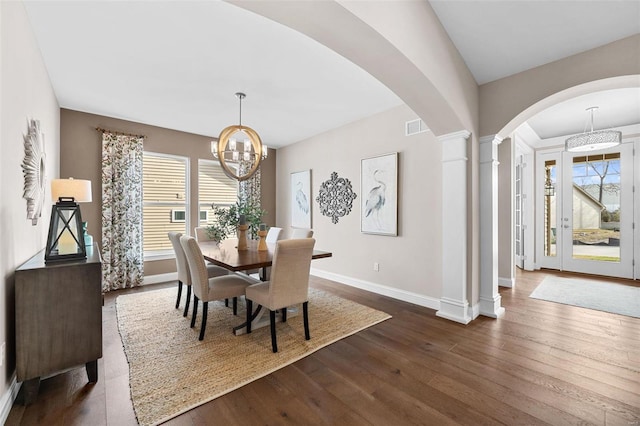 dining space with ornate columns, dark wood-type flooring, and a notable chandelier