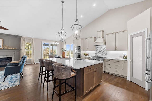 kitchen with a kitchen island with sink, hanging light fixtures, white cabinetry, stainless steel appliances, and custom exhaust hood