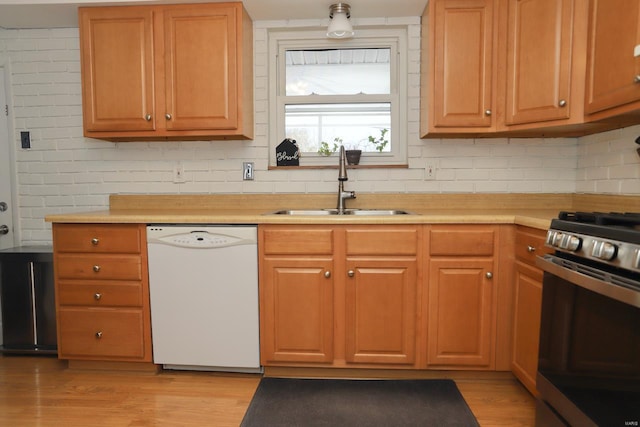 kitchen featuring sink, decorative backsplash, white dishwasher, stainless steel gas range, and light wood-type flooring