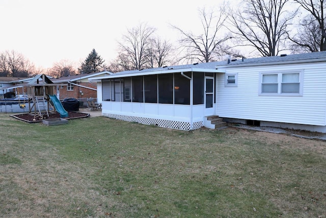 back house at dusk with a lawn, a sunroom, and a playground