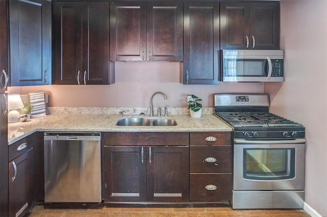 kitchen with stainless steel appliances, sink, dark brown cabinetry, and light stone counters