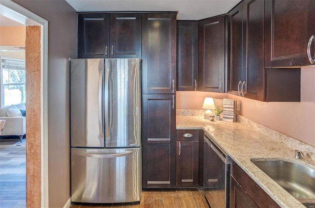 kitchen with stainless steel refrigerator, sink, dishwashing machine, light stone counters, and light hardwood / wood-style flooring