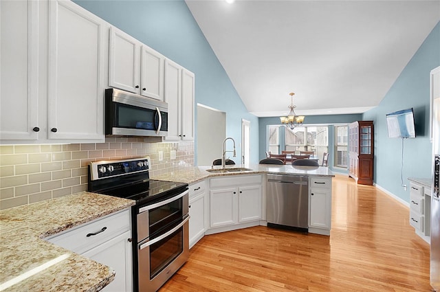 kitchen with vaulted ceiling, decorative light fixtures, sink, white cabinets, and stainless steel appliances