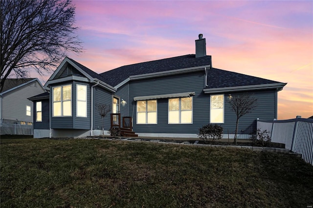 back house at dusk featuring a lawn