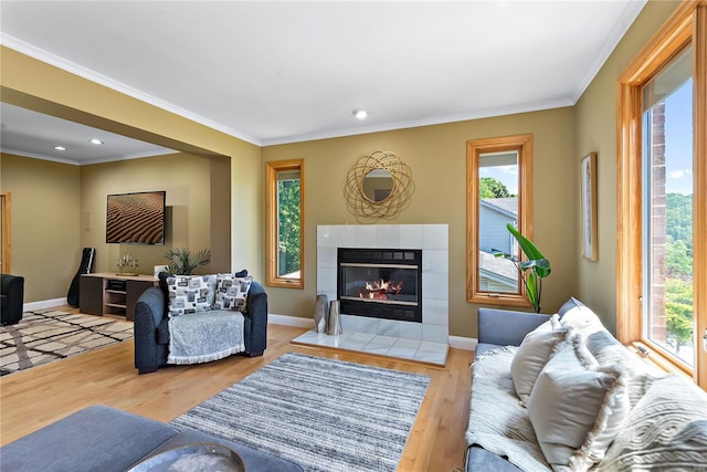 living room featuring a tiled fireplace, crown molding, and light wood-type flooring