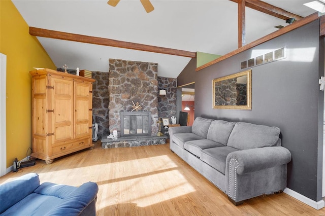 living area with baseboards, visible vents, lofted ceiling with beams, wood finished floors, and a stone fireplace