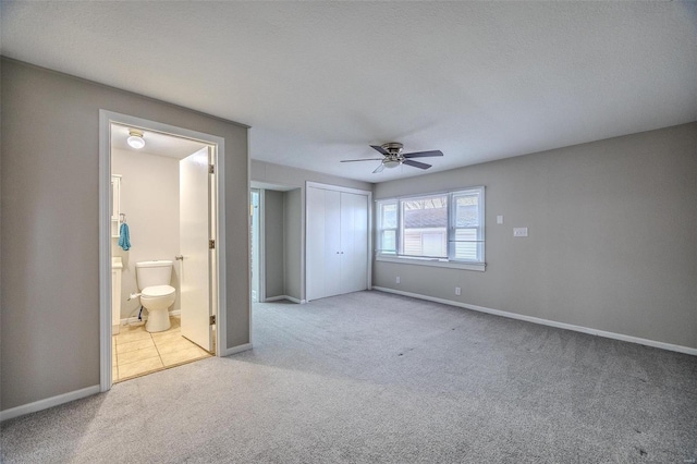 unfurnished bedroom featuring ceiling fan, a closet, connected bathroom, and light carpet