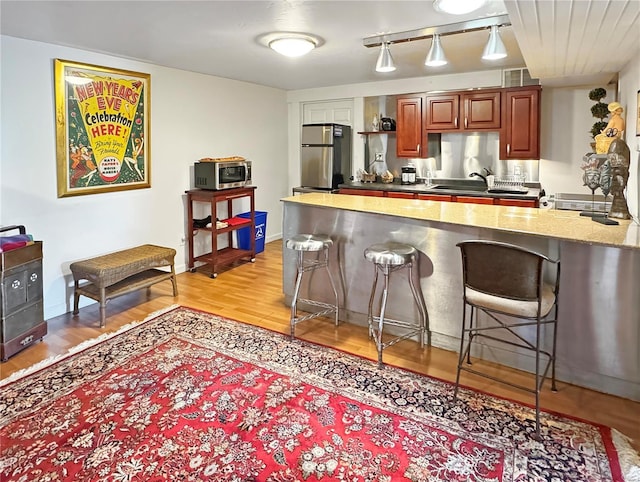 kitchen with a breakfast bar, sink, light hardwood / wood-style flooring, track lighting, and stainless steel appliances