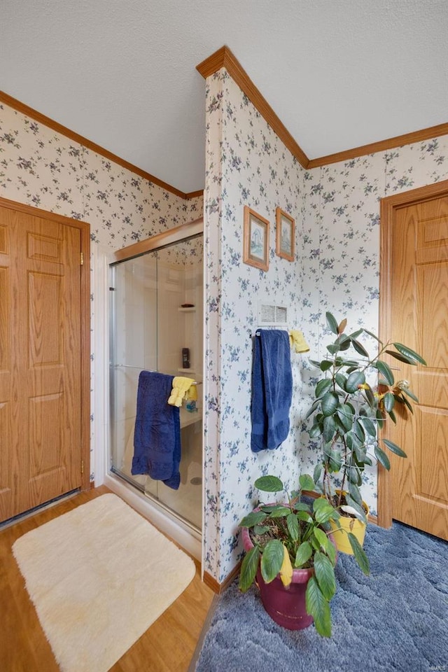 bathroom with hardwood / wood-style flooring, crown molding, an enclosed shower, and a textured ceiling