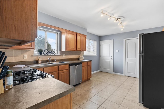 kitchen featuring light tile patterned flooring, stainless steel appliances, a sink, brown cabinetry, and dark countertops