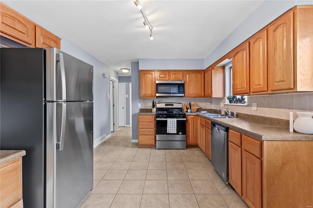 kitchen with light tile patterned floors, a sink, appliances with stainless steel finishes, tasteful backsplash, and brown cabinetry