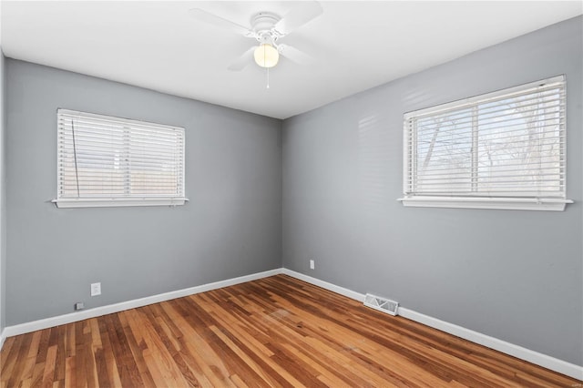 empty room with a ceiling fan, wood finished floors, visible vents, and baseboards