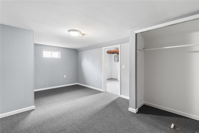 unfurnished bedroom featuring lofted ceiling, dark carpet, and baseboards