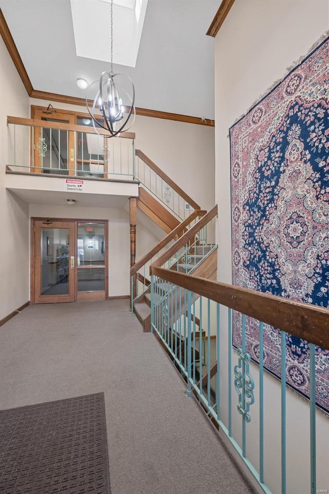 hall with crown molding, an inviting chandelier, a skylight, a high ceiling, and carpet floors