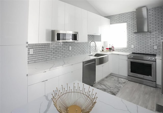 kitchen with sink, appliances with stainless steel finishes, light stone countertops, white cabinets, and wall chimney exhaust hood