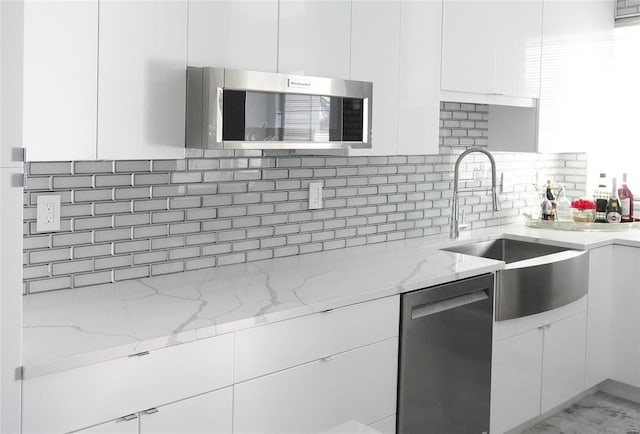 kitchen with light stone countertops, white cabinetry, appliances with stainless steel finishes, and sink