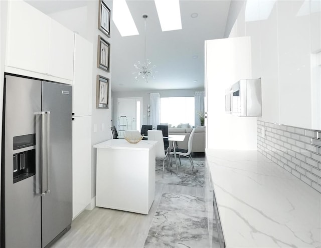 kitchen with high end fridge, hanging light fixtures, a notable chandelier, light stone countertops, and white cabinets