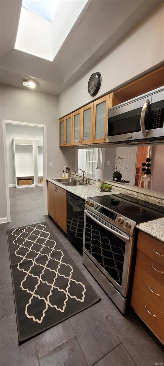 kitchen featuring light stone counters, sink, a skylight, and appliances with stainless steel finishes