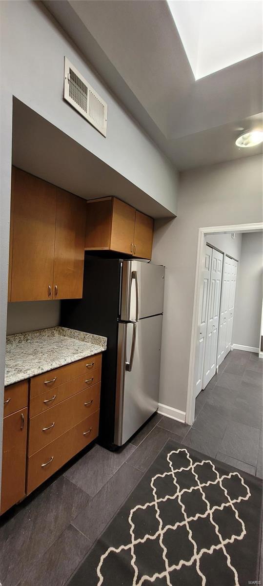 kitchen with light stone counters, dark tile patterned flooring, and stainless steel refrigerator