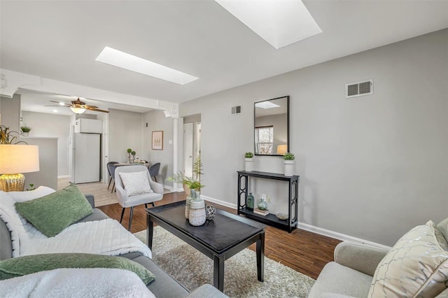 living room with ceiling fan, wood-type flooring, and a skylight