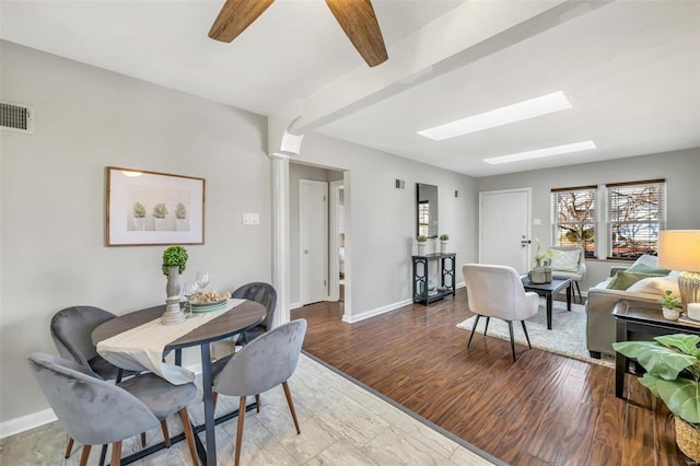 dining area with a skylight, decorative columns, ceiling fan, beam ceiling, and light hardwood / wood-style flooring