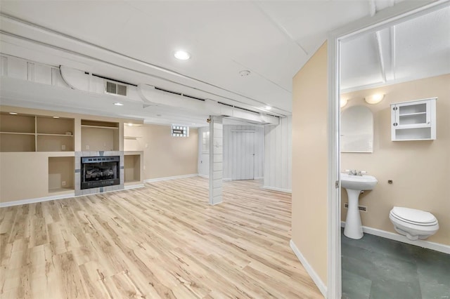 basement with a tile fireplace, wood-type flooring, and sink