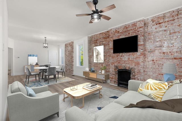 living room featuring a brick fireplace, ceiling fan, brick wall, and light wood-type flooring