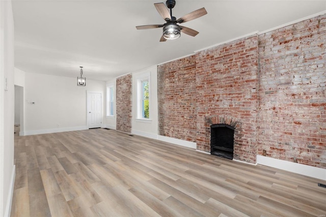 unfurnished living room with brick wall, ceiling fan with notable chandelier, a brick fireplace, and light hardwood / wood-style flooring