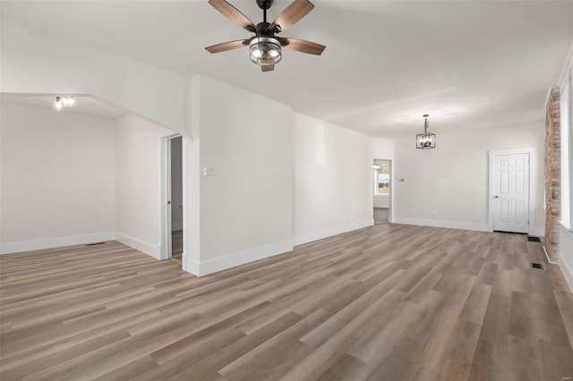 unfurnished living room with ceiling fan with notable chandelier and light hardwood / wood-style floors