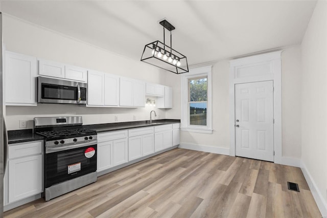 kitchen featuring decorative light fixtures, light hardwood / wood-style flooring, white cabinets, and appliances with stainless steel finishes