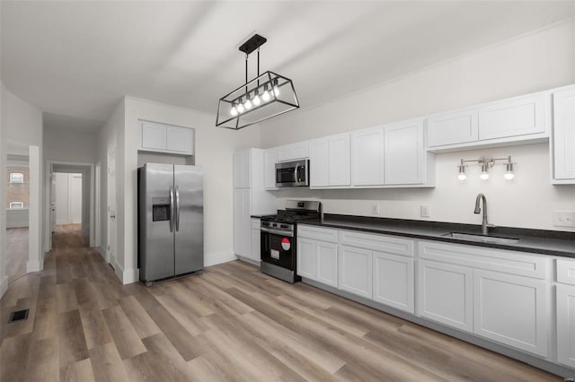 kitchen with appliances with stainless steel finishes, white cabinetry, sink, hanging light fixtures, and light hardwood / wood-style floors