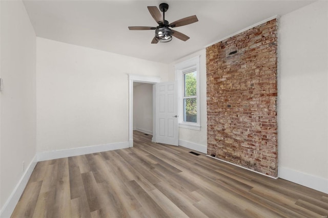 spare room with hardwood / wood-style flooring, ceiling fan, and brick wall