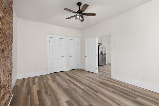 unfurnished bedroom featuring multiple closets, ceiling fan, stainless steel fridge with ice dispenser, and hardwood / wood-style flooring