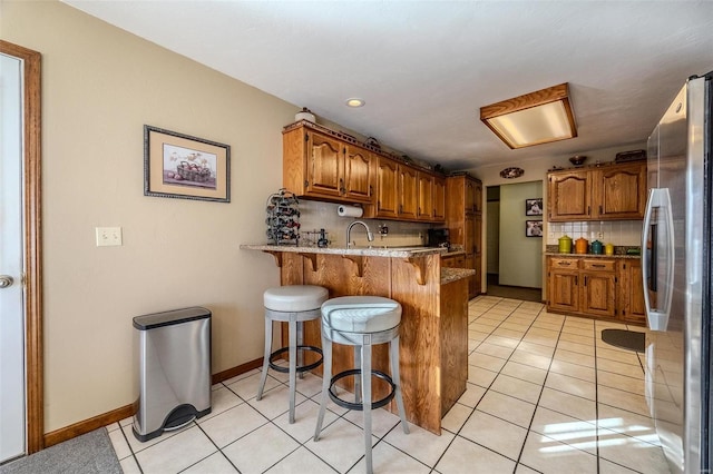 kitchen with a breakfast bar, stainless steel fridge, backsplash, light tile patterned floors, and kitchen peninsula