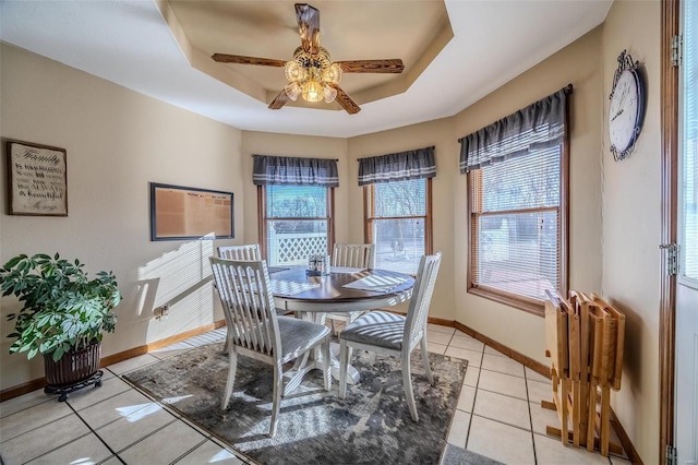 dining area featuring a raised ceiling, ceiling fan, and light tile patterned flooring