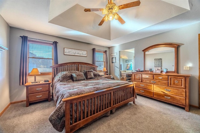 bedroom featuring multiple windows, a tray ceiling, light colored carpet, and ceiling fan