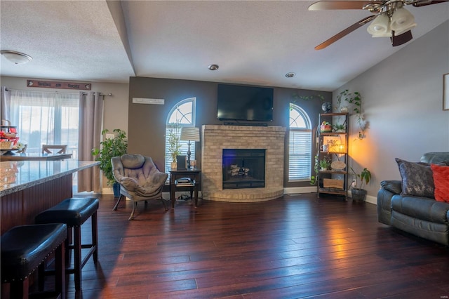 living room featuring vaulted ceiling, a brick fireplace, dark wood-type flooring, and a textured ceiling