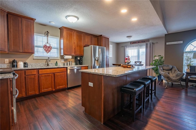 kitchen featuring light stone counters, stainless steel appliances, dark hardwood / wood-style floors, and a kitchen island